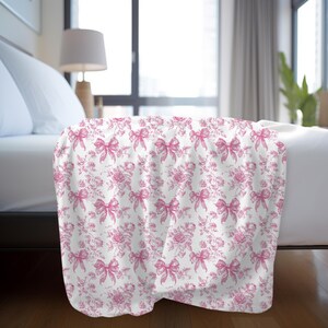Pink toile blanket with roses and bows design folded on bed