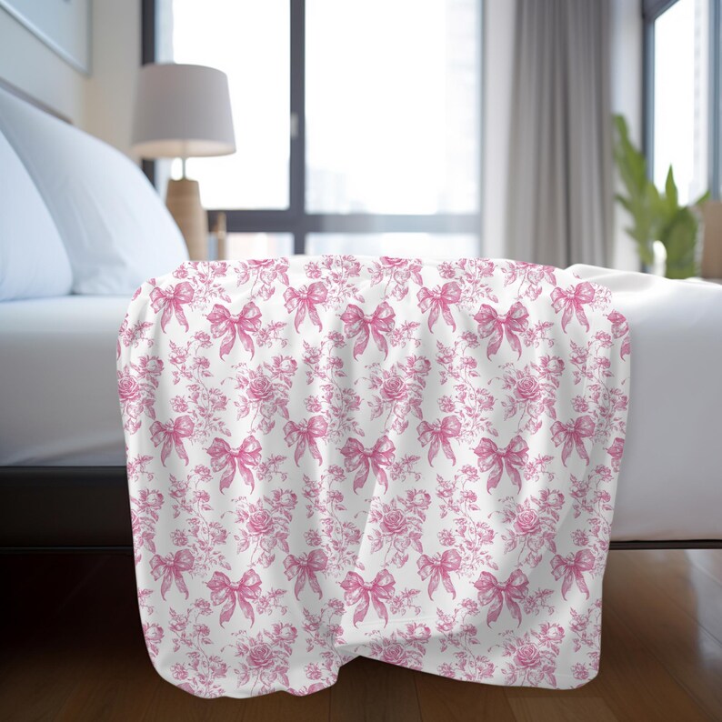 Pink toile blanket with roses and bows design folded on bed