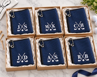 May include: Six navy blue waffle-textured golf towels, each featuring a white embroidered monogram and crossed golf clubs, attached to a black carabiner. Each towel is individually packaged in a square cardboard gift box with white tissue paper.