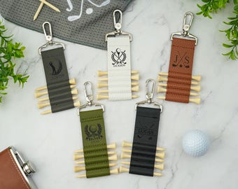 May include: Five personalized golf tee holders with different colors and designs. Each holder has a metal ring for attaching to a golf bag. The holders are made of leather and have a variety of engravings, including names, initials, and golf-related designs.