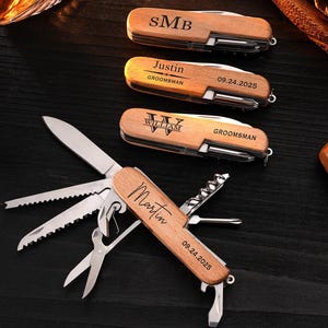 May include: Wooden multi-tool pocket knives with personalized engravings. One knife is open, displaying a blade, saw, scissors, and other tools. The closed knives have names and dates engraved on them. The knives are on a dark wooden surface.