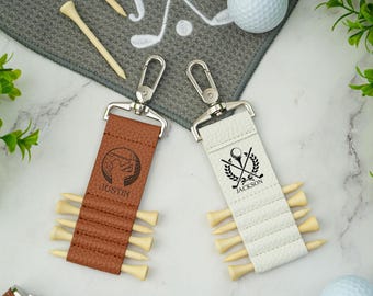 May include: Two golf tee holders with silver clasps. One is brown with "JUSTIN" and a golfer graphic, the other is white with "JACKSON" and a golf-themed emblem. Each holds several wooden golf tees.