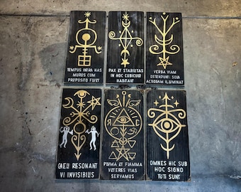 May include: Six rectangular wooden plaques with gold-colored symbols and Latin text. The plaques are arranged in two rows of three. The symbols include stars, eyes, and geometric shapes. The text is in white and is partially visible.