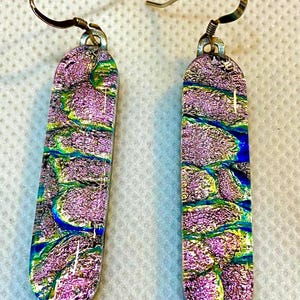 May include: A pair of dangle earrings with a rectangular shape. The earrings feature a colorful, abstract design with shades of pink, blue, green, and yellow. The earrings have silver-colored ear wires.