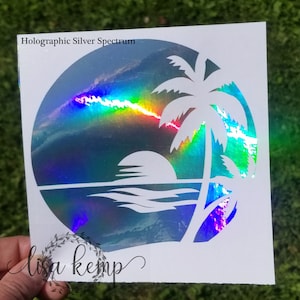May include: A holographic silver spectrum sticker featuring a tropical beach scene. The design includes a palm tree, sun, and ocean waves within a circular frame. The text "Holographic Silver Spectrum" is at the top, and the signature "lisa kemp" is at the bottom.