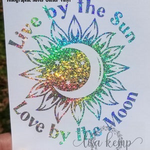 Peut inclure: Autocollant en vinyle paillet&eacute; argent&eacute; holographique avec le texte "Live by the sun love by the moon" et la signature "lisa kemp". L'autocollant pr&eacute;sente un motif de soleil et de lune avec un effet de paillettes arc-en-ciel.