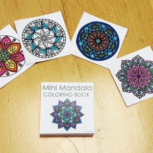 May include: A collection of colorful mandala designs on white squares and a mini coloring book. The designs feature intricate patterns in various colors, including pink, orange, blue, and green. The book cover displays a mandala design with the text "Mini Mandala Coloring Book".