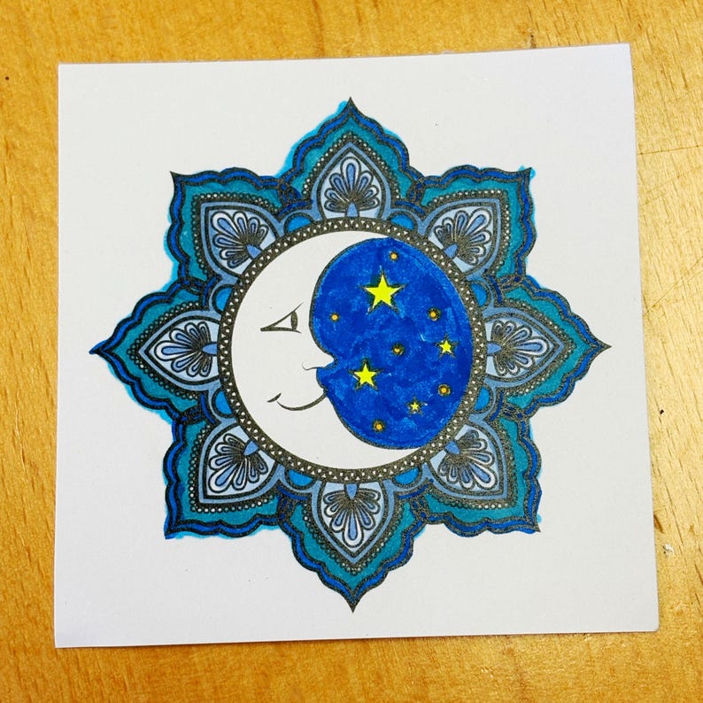 May include: A white square card featuring a celestial design. The central image is a crescent moon with a smiling face, set against a dark blue starry sky. The moon is surrounded by a teal and blue floral mandala.