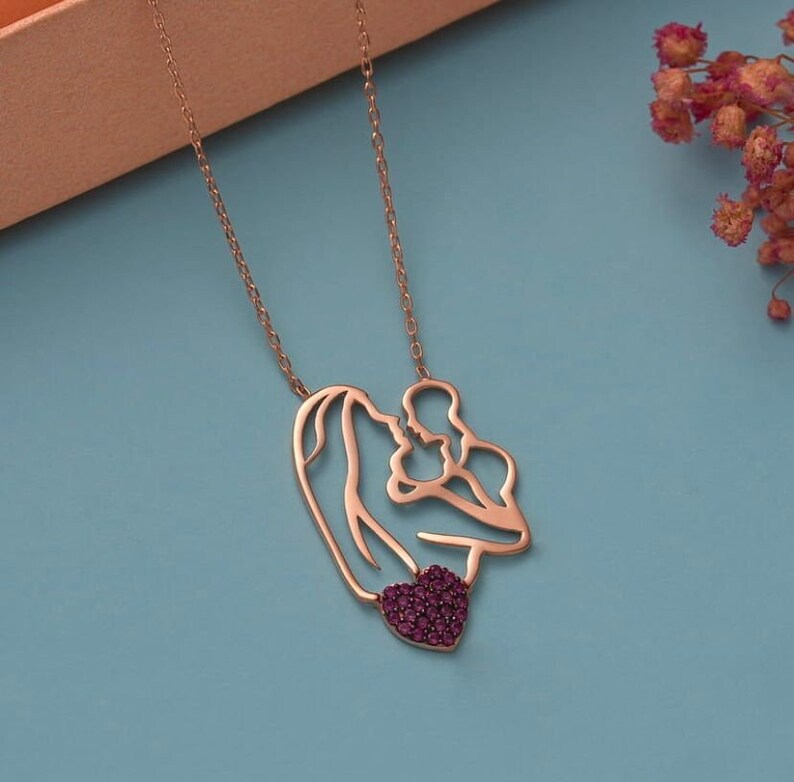 This necklace portrays a mother holding her baby under a red heart. Symbolizing love and maternal connection, it's a meaningful accessory suitable for any occasion