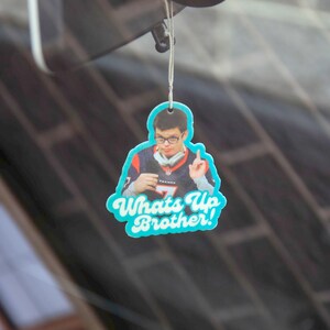 May include: A blue and white car air freshener with a photo of a person wearing a jersey and the text "Whats Up Brother!"