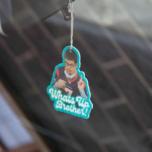 May include: A blue and white car air freshener with a photo of a man wearing a jersey and the text "Whats Up Brother!"