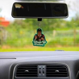 May include: A green car air freshener with a photo of a person wearing a jersey and the text "What's Up Brother!" hanging from the rearview mirror of a car.