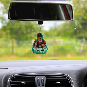 May include: A teal car air freshener with a photo of a man wearing a blue and white jersey. The text on the air freshener reads "Whats Up Brother!"