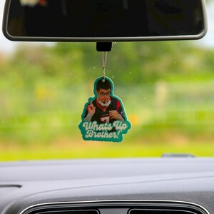 May include: A teal car air freshener with a picture of a man wearing a baseball jersey and the text "Whats Up Brother!"