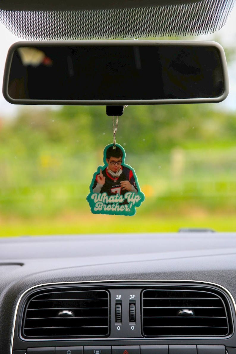 May include: A teal car air freshener with a picture of a man wearing a baseball jersey and the text "Whats Up Brother!"