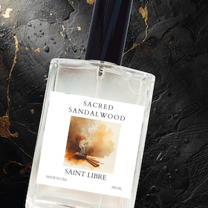 May include: A clear rectangular perfume bottle with a black cap. The label reads "SACRED SANDALWOOD" and "SAINT LIBRE" with an image of incense. The bottle contains 100 mL of perfume and is labeled "MADE IN USA".