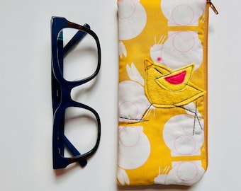 May include: A pair of dark blue eyeglasses next to a yellow glasses case. The glasses case has a yellow background with white circles and a yellow bird applique with a pink beak. The case has a gold zipper.