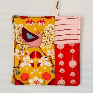 Puede incluir: Manopla de cocina cuadrada de patchwork con aplique de pájaro. El aplique de pájaro es amarillo, burdeos y azul. El patchwork incluye patrones florales y geométricos en tonos amarillos, rosas y rojos. Se adjunta un lazo color crema para colgar.