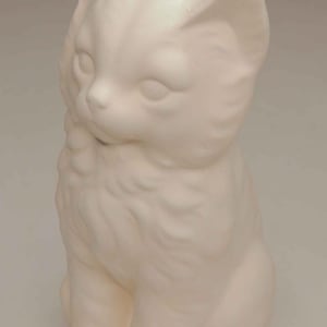May include: A matte white ceramic figurine of a sitting kitten. The sculpture features molded fur texture, pointed ears, and a smooth, unpainted surface. The kitten is depicted in a seated position with its head turned slightly to the left side.
