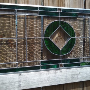 May include: A rectangular stained glass panel featuring a central circular motif with an internal diamond shape. The design incorporates deep green glass borders and clear textured glass panes held together by thin silver metal lead lines.