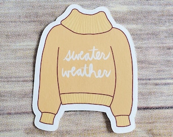 May include: A yellow sweater with a turtleneck and the text "sweater weather" printed on the front.