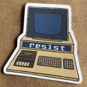 May include: A sticker featuring a retro computer design with a blue screen and the word "resist" displayed. The sticker has a beige background and a black border, with a keyboard and cassette player.