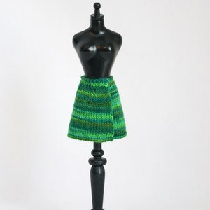 May include: A green and black striped knitted skirt on a black mannequin stand.