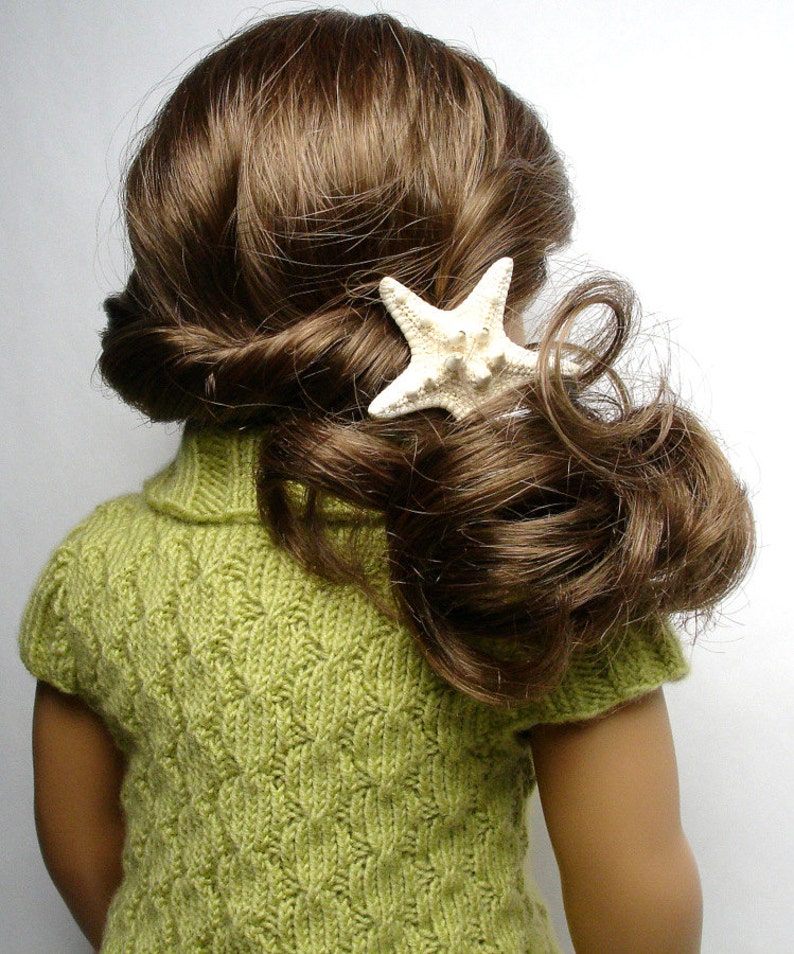 Pu&ograve; includere: Una bambola con lunghi capelli castani che indossa un maglione di lana verde con un fermaglio per capelli a forma di stella marina bianca.
