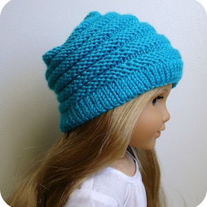 May include: A turquoise knitted hat with a textured pattern. The hat is worn by a doll with long blonde hair.