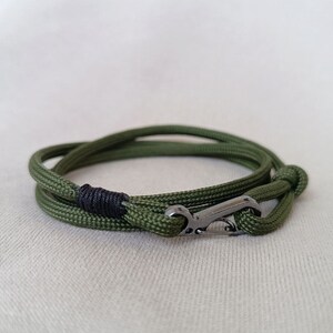 Op de afbeelding: Een groene paracord armband met een zwarte accent en een zilveren haak sluiting.