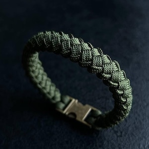 Può includere: Un braccialetto in paracord verde con una chiusura argentata. Il braccialetto è intrecciato con un motivo stretto e intricato.