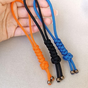 May include: Three keychains made with colourful paracord and metal beads. The keychains are orange, black, and blue.