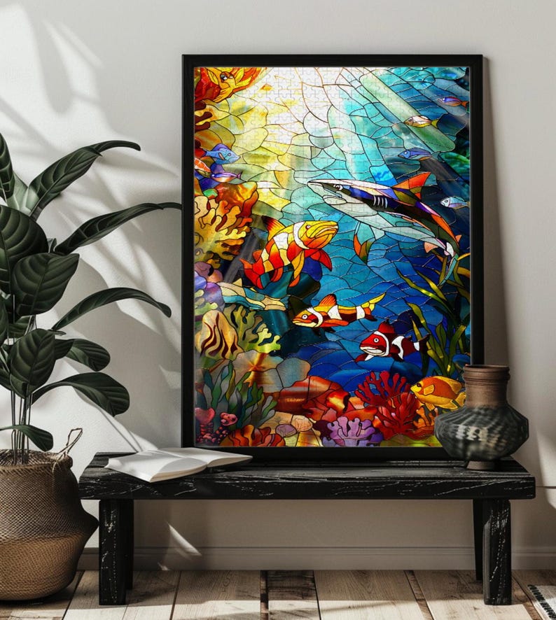 May include: A framed stained glass artwork depicting an underwater scene. The artwork features colorful fish, coral, and a shark against a blue and yellow background. The frame is black.