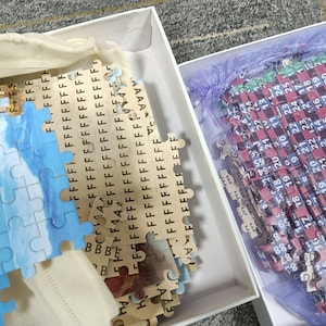 May include: Two boxes containing partially completed jigsaw puzzles. One puzzle features a blue and white sky scene, the other has a red, black, and blue checkered pattern with numbers.