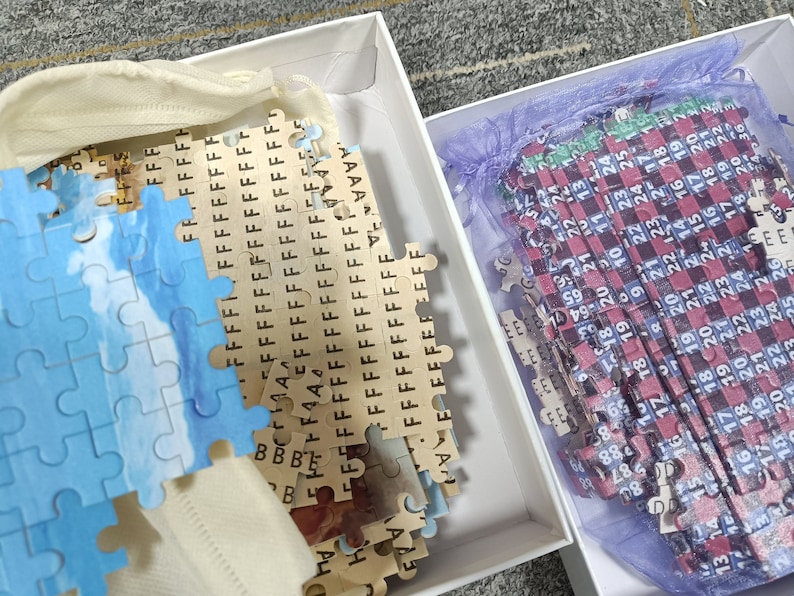 May include: Two boxes containing partially completed jigsaw puzzles. One puzzle features a blue and white sky scene, the other has a red, black, and blue checkered pattern with numbers.