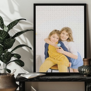 May include: Two young girls, one wearing a yellow dress and the other wearing a blue and white dress, are hugging each other. The girl in the yellow dress is holding a blue egg.