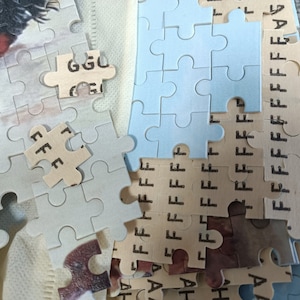 May include: A close-up of a partially completed jigsaw puzzle with blue and beige pieces. The pieces have letters printed on them, including "GGU", "FFF", and "FFFFF".
