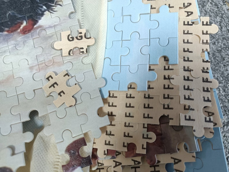 May include: A close-up of a partially completed jigsaw puzzle with blue and beige pieces. The pieces have letters printed on them, including "GGU", "FFF", and "FFFFF".