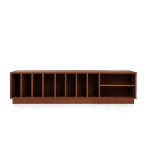 May include: A long, rectangular, dark brown wooden storage cabinet with multiple vertical compartments and two shelves. The cabinet is designed for organizing items and has a modern, minimalist aesthetic.