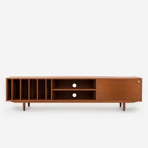May include: A mid-century modern wooden media console in a warm brown finish. It has open storage, shelves, and a sliding door. The console is supported by tapered legs and has a brass-coloured knob.