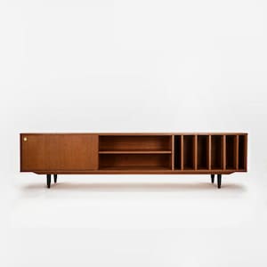 May include: A mid-century modern wooden media unit with a sliding door, open shelving, and vertical dividers. The brown console has black legs and a gold-coloured knob. The unit is approximately 183 cm long.