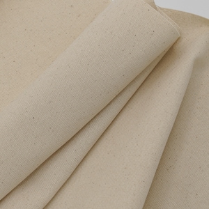 May include: Close-up of a natural, off-white canvas fabric with a subtle texture. The fabric is folded and shows the weave of the material.