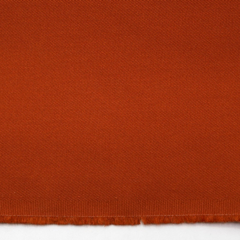 May include: A close-up of a piece of orange fabric with a textured weave. The fabric has a raw edge.