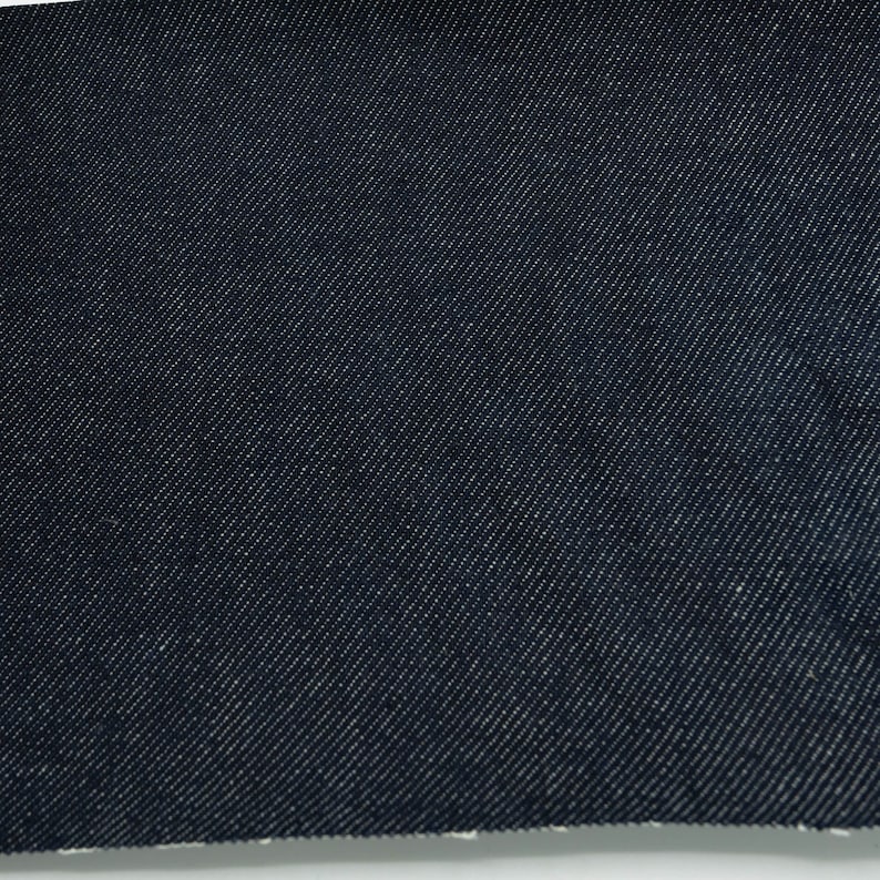 May include: Close-up of a dark blue denim fabric with a diagonal weave pattern.