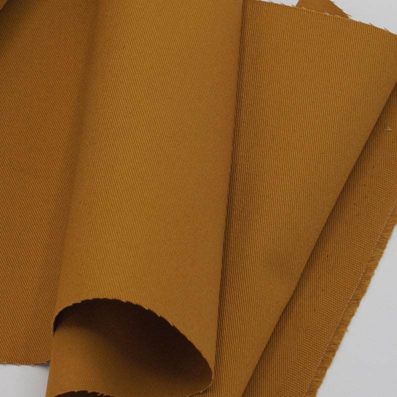 May include: Close-up of a folded piece of brown cotton fabric with a subtle texture. The fabric has a slightly rough, woven appearance.