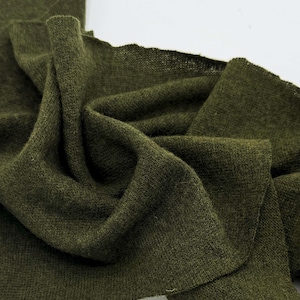 May include: A piece of olive green fabric with a fine knit texture. The material is draped in soft folds, showcasing the consistent dark green color and the subtle, slightly translucent quality of the knit weave across the entire surface.