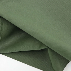 May include: Close-up of olive green fabric with a diagonal weave. The fabric is folded over, revealing a layered effect and highlighting the texture and color variations. The material appears to be a medium-weight cotton or blend, suitable for apparel or home decor.