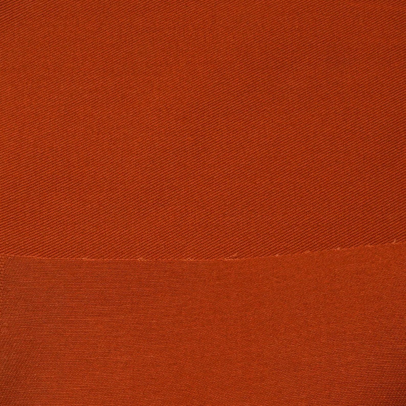 May include: A close-up of a rust-colored fabric with a subtle diagonal weave pattern. The fabric has a smooth, slightly textured surface.