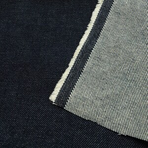 May include: Close-up of dark blue denim fabric with a white selvedge edge. The fabric is woven with a diagonal twill pattern.