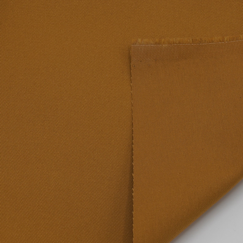 May include: A close-up of a brown fabric with a diagonal weave. The fabric is folded over on itself, showing the raw edge.